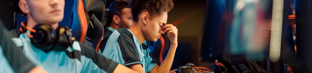 Un giocatore di eSport deluso reagisce dopo una partita competitiva difficile, mentre i compagni di squadra continuano a giocare su PC da gioco professionali in un'arena di eSport.